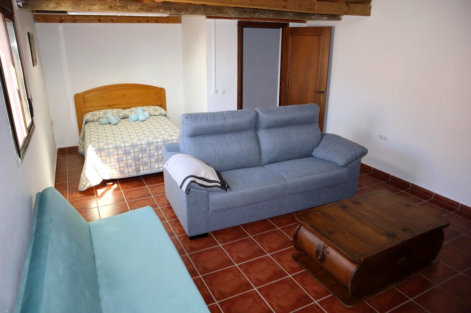 Dormitorio con cama, sofá y vigas de madera vistas