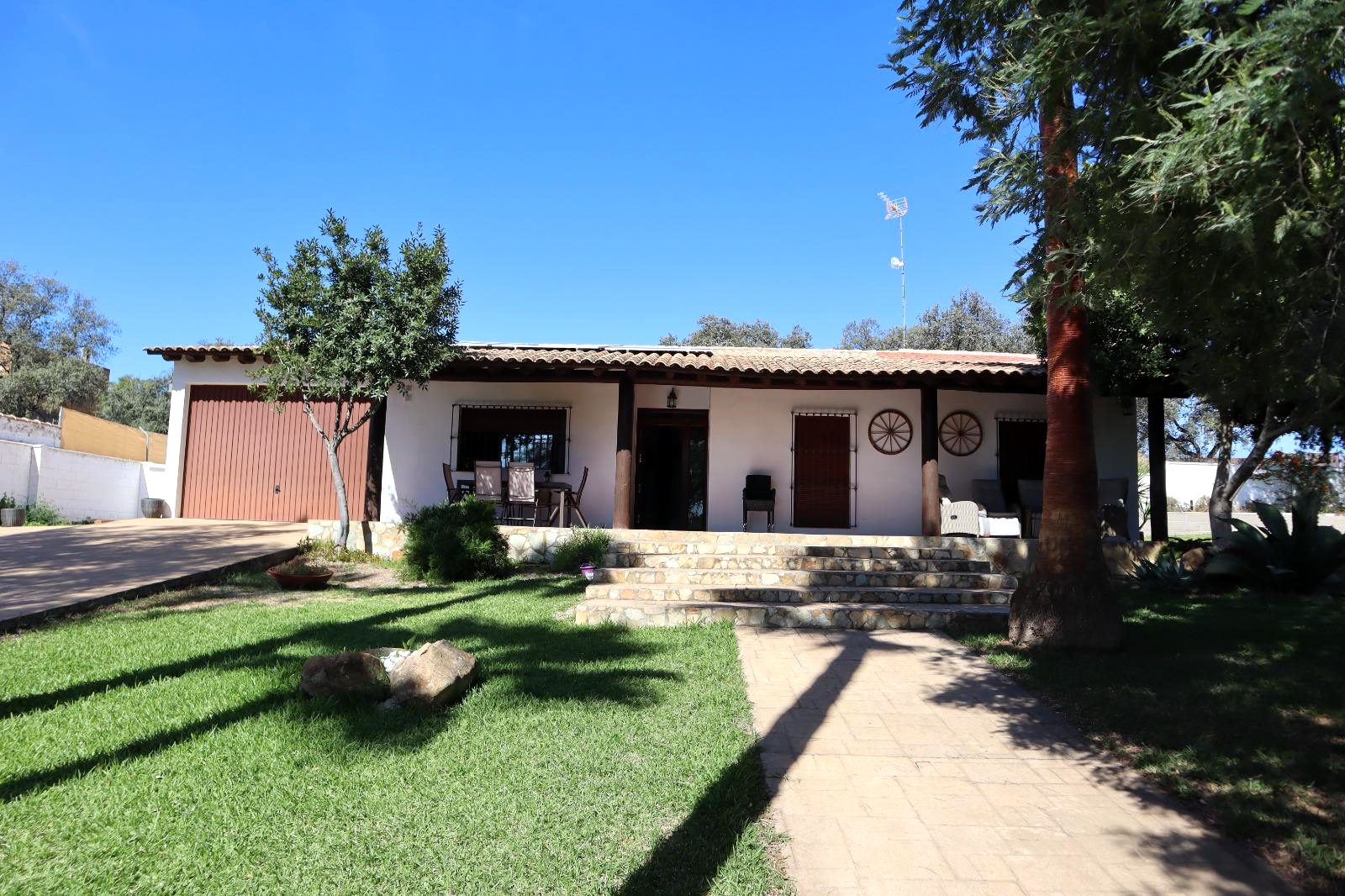 Fachada de la finca con jardín y árboles al sol de la tarde