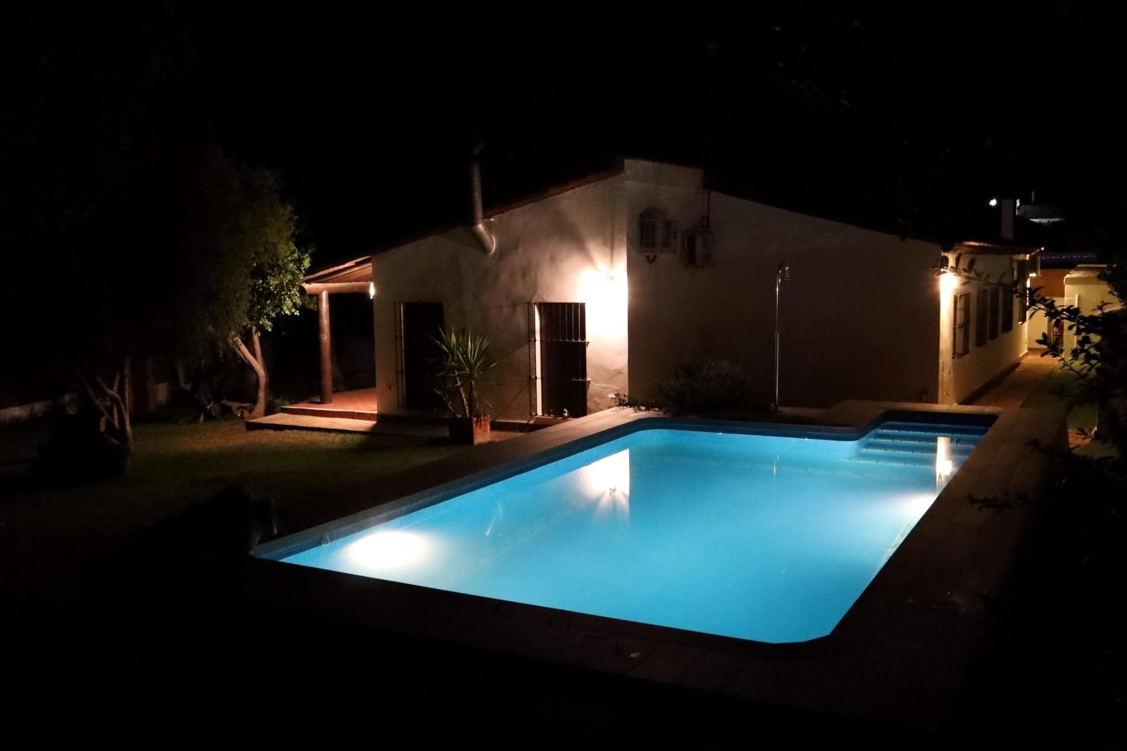 Piscina iluminada por la noche con la casa al fondo